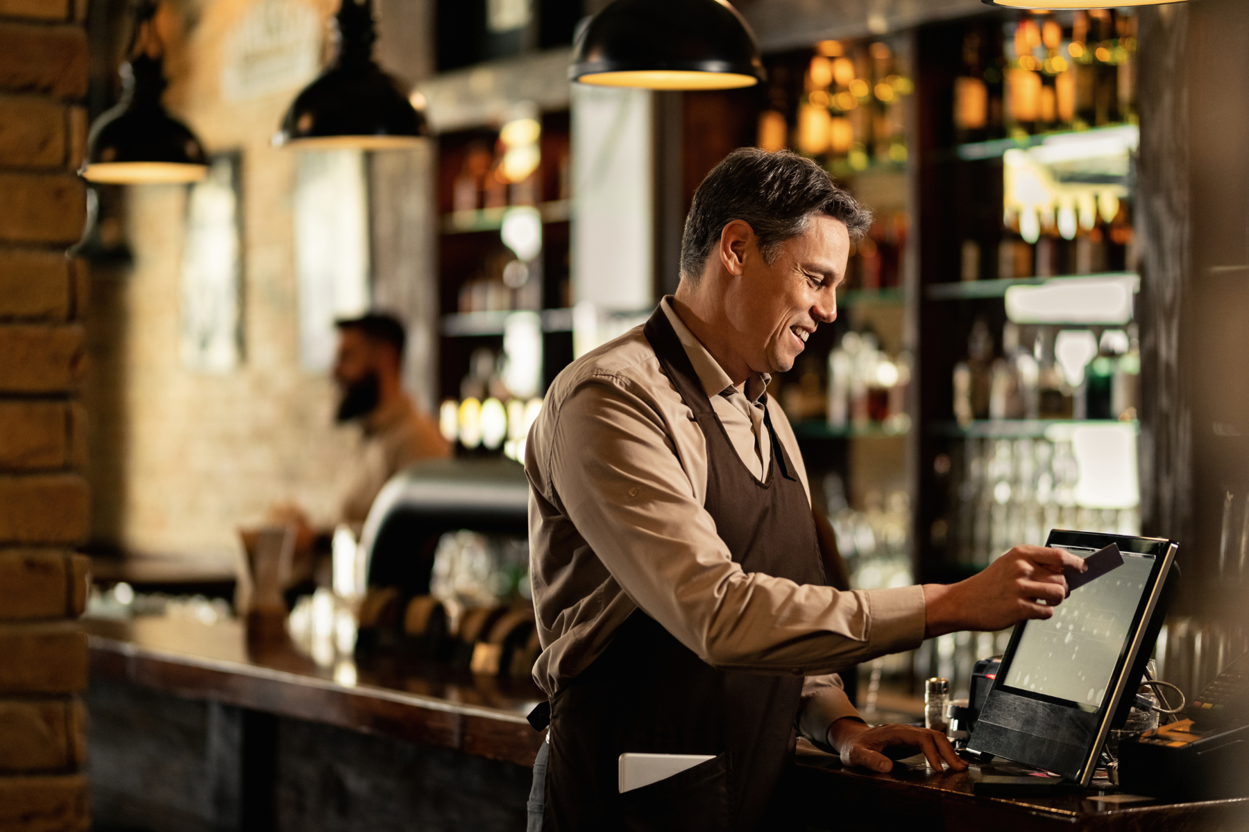 Smiling bartender using a POS system at a bar, processing a payment.